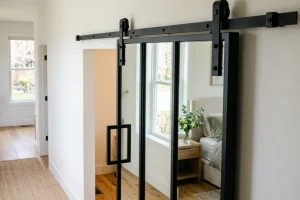 Black sliding barn door on an overhead track, installed at the entrance to a cozy bedroom.